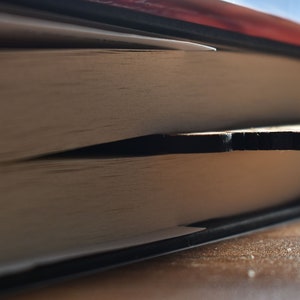 May include: A close-up of a book with a wooden bookmark sticking out of the pages. The book is closed and the bookmark is visible.
