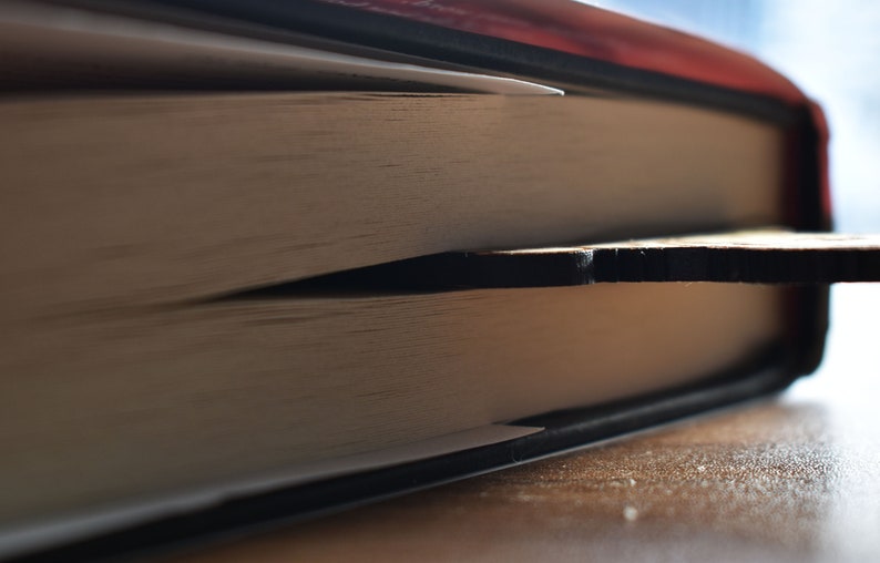 May include: A close-up of a book with a wooden bookmark sticking out of the pages. The book is closed and the bookmark is visible.