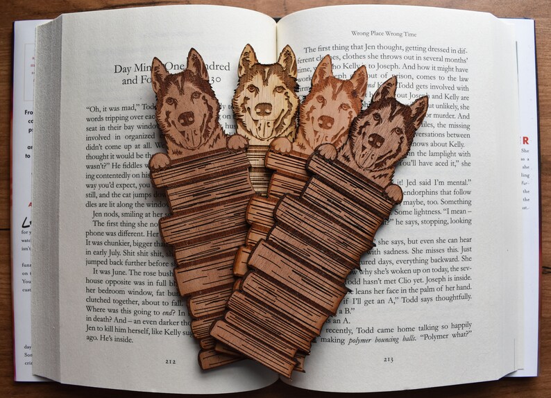 May include: Four wooden bookmarks featuring a dog peeking over a stack of books. The bookmarks are made of light brown wood with a detailed engraved design.