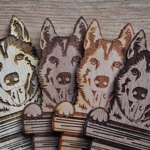 May include: Four wooden dog ornaments, each with a different wood grain pattern. The dogs are all facing forward with their tongues sticking out. They are all holding a wooden plank in their paws.