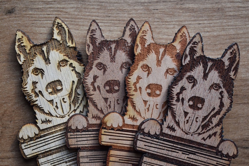 May include: Four wooden dog ornaments, each with a different wood grain pattern. The dogs are all facing forward with their tongues sticking out. They are all holding a wooden plank in their paws.