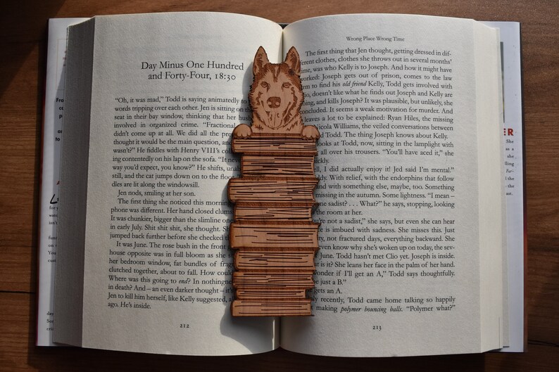 May include: A wooden bookmark featuring a German Shepherd dog standing on a stack of books. The bookmark is a light brown color and has a detailed design. The dog is looking to the right and has a friendly expression. The bookmark is a great gift for dog lovers and bookworms.