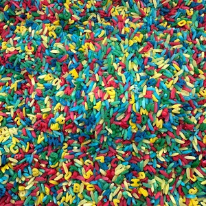 May include: A close-up of a pile of colorful rice with letters printed on each grain. The rice is a mix of red, yellow, blue, and green.