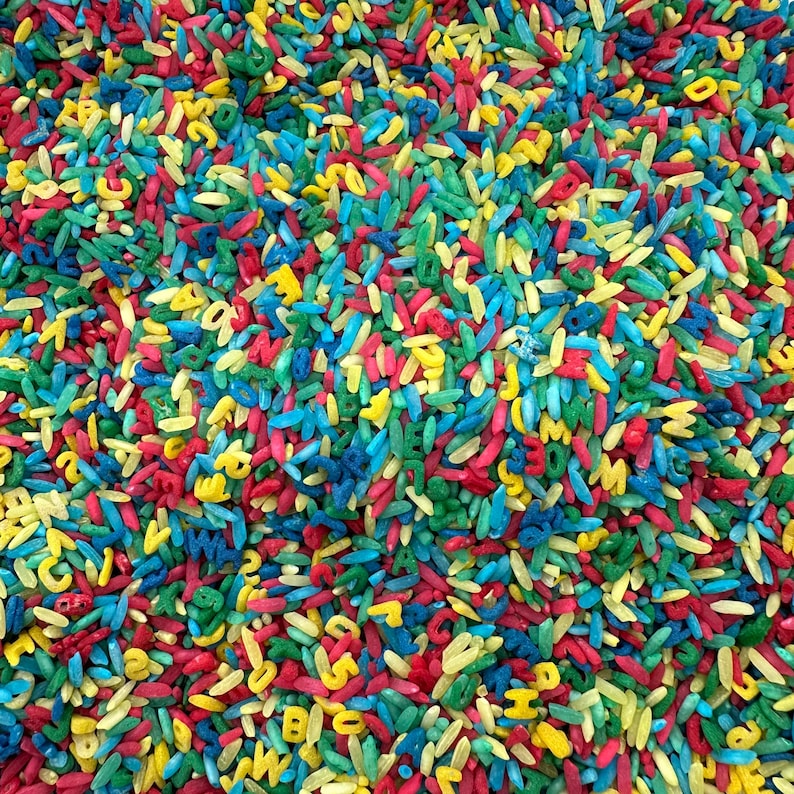 May include: A close-up of a pile of colorful rice with letters printed on each grain. The rice is a mix of red, yellow, blue, and green.