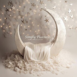 Puede incluir: Un accesorio de fotografía de recién nacido en forma de media luna blanca, con un tejido blanco en el interior y pétalos de flores blancas esparcidos alrededor de la base. El fondo es gris claro con nubes blancas y estrellas doradas.