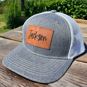 May include: A grey and white trucker hat with a brown leather patch that says "Jackson" on it.