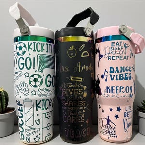 Pode incluir: Três canecas isoladas com vários designs. Uma é branca com gráficos de futebol e o texto "KICK IT! GO!". Outra é preta com texto temático de professor e um gráfico de maçã. A terceira é rosa com texto temático de dança e silhuetas.