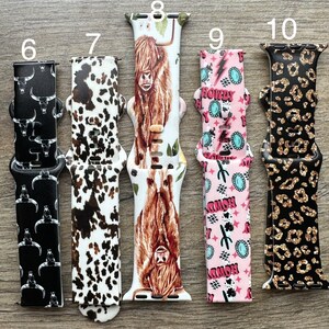 May include: Five different Apple Watch bands with various patterns. The bands are numbered 6 through 10. Band 6 is black with white skulls, band 7 is white with brown and black spots, band 8 is white with a brown Highland Cow, band 9 is pink with turquoise and white lightning bolts and the word "Howdy" repeated, and band 10 is black with gold glitter and leopard spots.