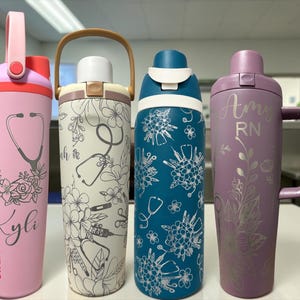 May include: Four insulated water bottles with carrying handles. The first is pink with a stethoscope and flower graphic and the name Kyli. The second is cream with medical icons and flowers. The third is blue with floral patterns. The fourth is purple with the name Amy RN.
