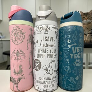 May include: Three cylindrical water bottles with flip-top lids. The left bottle is pink with anatomical illustrations. The centre white bottle features the text "I SAVE ANIMALS WHATS YOUR SUPER POWER?" and veterinary icons. The right blue bottle has "VET TECH" text and various pet-related graphics.