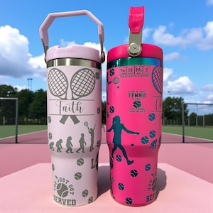 Puede incluir: Dos vasos aislados de acero inoxidable con diseños temáticos de tenis. Uno es rosa claro con raquetas de tenis, la palabra "Faith" y gráficos de pelotas de tenis. El otro es rosa intenso con pelotas de tenis, una silueta de jugador de tenis y el texto "A day without tennis is like..."