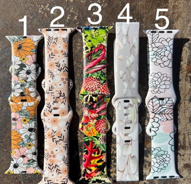 May include: Five different Apple Watch bands with floral patterns. The bands are numbered 1 through 5. The bands are all white with different floral patterns.