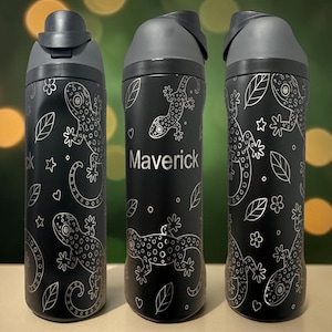 May include: Three black water bottles with gray lids, each featuring a white line-art pattern of lizards, leaves, flowers, and small hearts. The center bottle displays the name Maverick in white text, while the others show the lizard design.