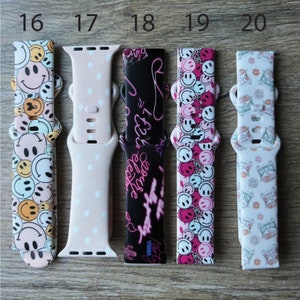 May include: Five different Apple Watch bands with various patterns. The bands are pink with smiley faces, pink with white polka dots, black with pink neon writing, pink and black with smiley faces, and white with a black and gray pattern.