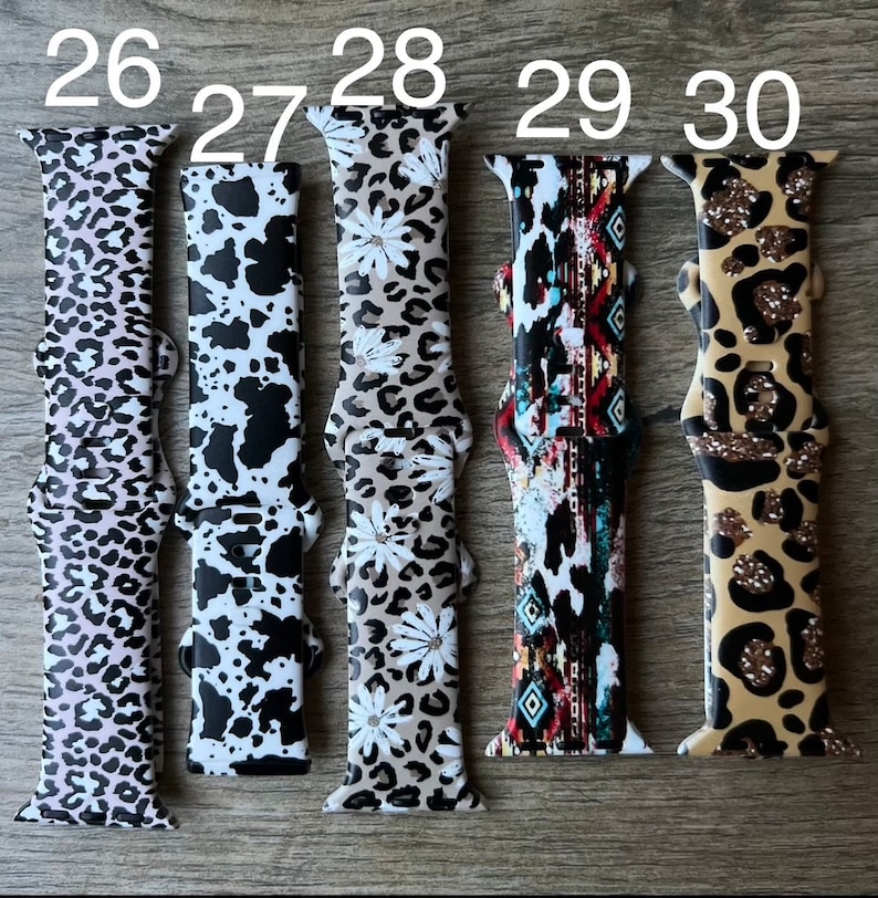 May include: Five different patterned Apple Watch bands. The bands are in a variety of colors and patterns, including leopard print, floral, and geometric. The bands are numbered 26 through 30.