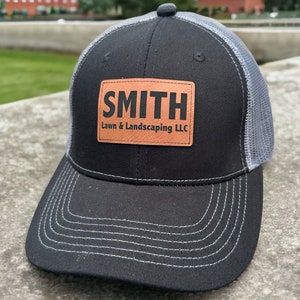 May include: Black and grey trucker hat with a brown leather patch that says "SMITH Lawn & Landscaping LLC."