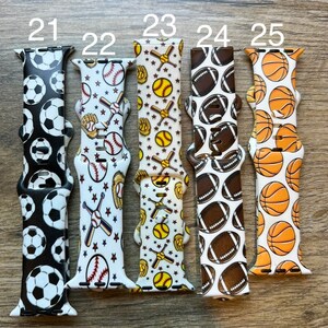 May include: Five different Apple Watch bands with various sports-themed patterns. The bands are white with black, brown, or orange accents. The patterns include soccer balls, baseballs, softballs, footballs, and basketballs.