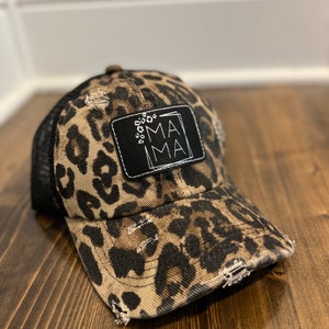 May include: A brown and black leopard print trucker hat with a black patch that says "MAMA" in white lettering.