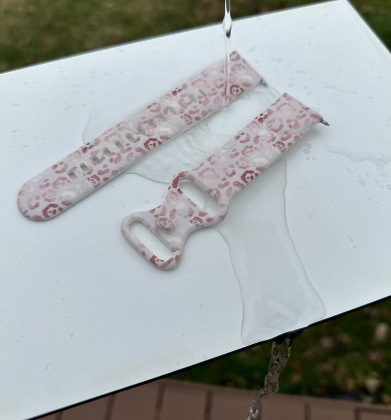 May include: Two-piece watch strap in a light pink hue, featuring a leopard print pattern in brown and pink. The strap is wet, with water droplets visible. The watch strap is designed to be waterproof.
