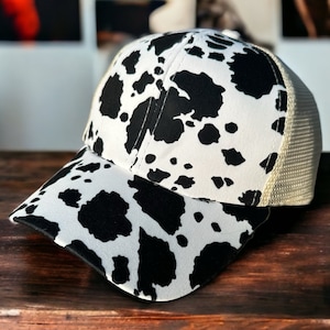 Può includere: Un cappello da baseball con stampa a mucca bianco e nero con retro in rete.