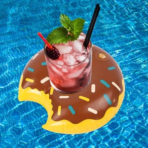 May include: A brown and yellow inflatable donut pool float with sprinkles, holding a glass of red drink with ice and a sprig of mint. The drink has a black straw.