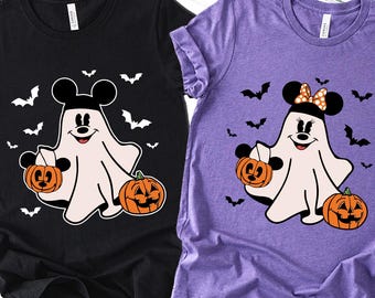 May include: Black and purple t-shirts with Halloween-themed graphics. Each shirt features a cartoon ghost character with Mickey Mouse ears, holding a pumpkin. Bats and pumpkins decorate the background.