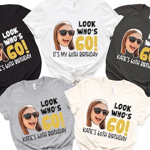 May include: Five different color t-shirts with a photo of a person wearing sunglasses and the text "Look Who's 60!" and "Katie's 60th Birthday" printed on them.