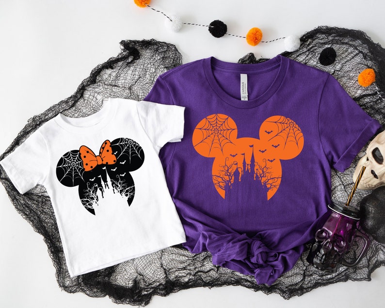 May include: Two white t-shirts with a black and orange Halloween Mickey Mouse design. The larger shirt has a purple background and the smaller shirt has a white background.