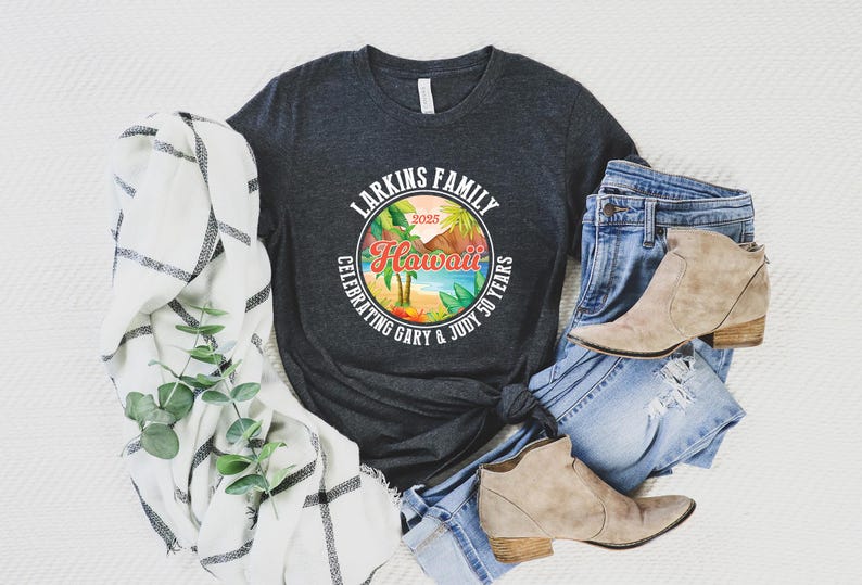 May include: A dark gray t-shirt with a colorful Hawaii graphic, jeans, and tan ankle boots. The graphic reads "Larkins Family Hawaii Celebrating Gary & Judy 50 Years 2025". A white and black plaid scarf and greenery are also in the image.