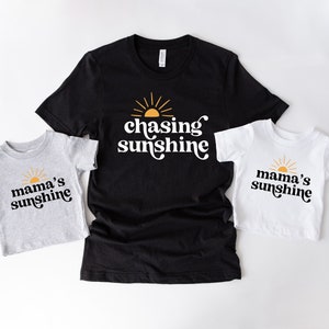 May include: Three t-shirts with a sun and text. The black t-shirt says "chasing sunshine". The grey t-shirt says "mama's sunshine". The white t-shirt says "mama's sunshine".