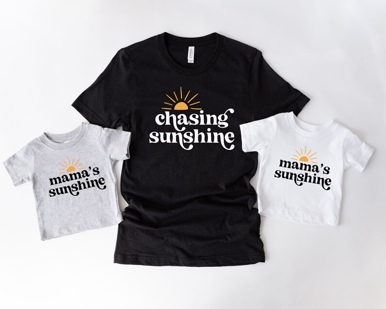 May include: Three t-shirts with a sun and text. The black t-shirt says "chasing sunshine". The grey t-shirt says "mama's sunshine". The white t-shirt says "mama's sunshine".
