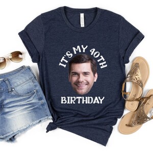 May include: A navy blue t-shirt with the text "It's my 40th Birthday" in white. A man's face is in the center of the text.
