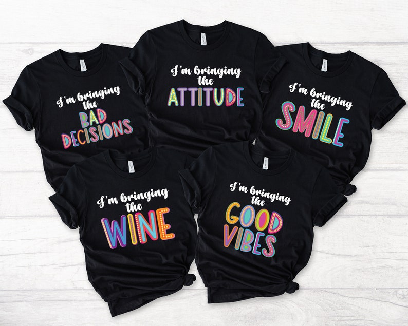 May include: Five black t-shirts with colorful text. The shirts say "I'm bringing the BAD DECISIONS", "I'm bringing the ATTITUDE", "I'm bringing the SMILE", "I'm bringing the WINE", and "I'm bringing the GOOD VIBES".