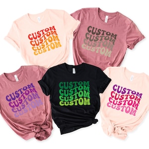 May include: Five t-shirts with the word "CUSTOM" repeated in a retro font in different colors. The shirts are in various colors, including pink, black, and brown.