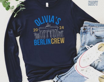 May include: Navy blue long-sleeve t-shirt with a white graphic of the Brandenburg Gate and the text "Olivia's 20 24 Berlin Crew".
