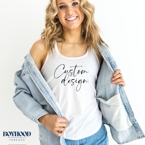 May include: White tank top with the text "Custom design" in black script font. The model is wearing a light blue denim jacket and blue denim shorts.