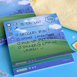 May include: A square sticky note pad featuring a blue sky and green field background with a computer desktop interface design. The text reads TO DO LIST, 7/26, GROCERY RUN, UPDATE CALENDAR, PICK UP PET FOOD, DINNER @ 6PM W/ LAUREN, and 1:00 A.M.