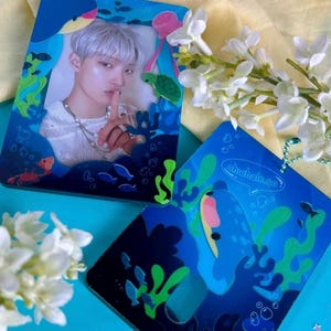 May include: Two blue and green acrylic charms with a sea-life theme. One charm features a photo of a person with a finger to their lips, surrounded by sea creatures. The other charm features a whale with a speech bubble that says "ohwhale.co".