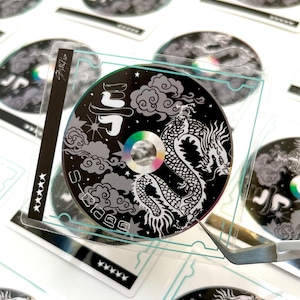 May include: A clear plastic sheet with a black and white sticker featuring a dragon with clouds and stars. The sticker has the text "Stage" and "J5" on it.