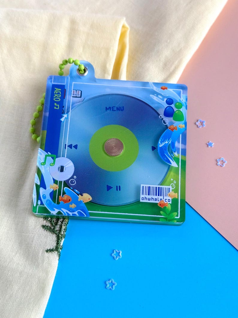 K&ouml;nnte beinhalten: Ein klarer Acryl-Schl&uuml;sselanh&auml;nger mit einem CD-Design in Gr&uuml;n und Blau. Der Schl&uuml;sselanh&auml;nger hat eine gr&uuml;ne Perlenkette und enth&auml;lt den Text "AERO" und "MENU". Kleine orangefarbene Fische und Blasen verzieren das Design. Der Text "ohwhale.co" ist ebenfalls sichtbar.