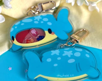 Può includere: Due portachiavi a forma di balena blu con catene dorate. Una balena è piena di glitter colorati e l'altra ha stelle bianche. La balena in basso ha il testo "ohwhale co".
