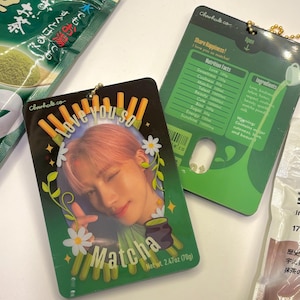 May include: A green and black keychain with a photo of a person and the text "Love you so Matcha" and "Net wt. 2.47oz (70g)". The keychain also has a green and black card with the text "Chiwhale.co Share Happiness! I love you so matcha!" and a nutrition facts label.