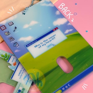 May include: A decorative tag with a whimsical computer-themed design. The tag features a blue sky and green field background with a pop-up window that reads "Who is the owner of my heart!?" and the word "you!" A pink mouse shape is cut out.