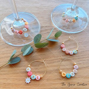 May include: Set of four gold-toned wine glass charms with colorful beads spelling out the names "Allison", "Erika", "Kate", and "Wendy". Each charm has a small white flower attached.