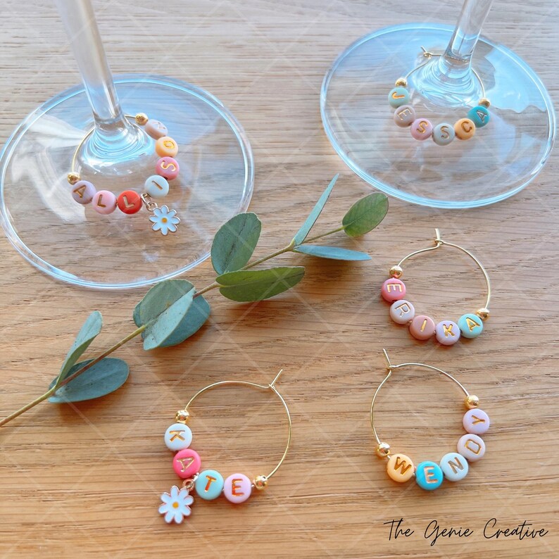 May include: Set of four gold-toned wine glass charms with colorful beads spelling out the names "Allison", "Erika", "Kate", and "Wendy". Each charm has a small white flower attached.