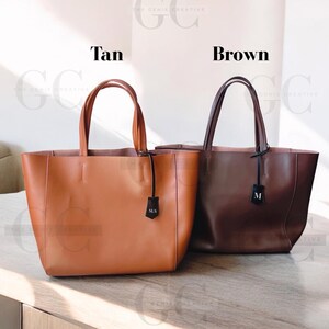 May include: Two leather tote bags, one tan and one brown, with personalized initials on a leather tag. The tan bag has the initials "MLS" and the brown bag has the initial "M".