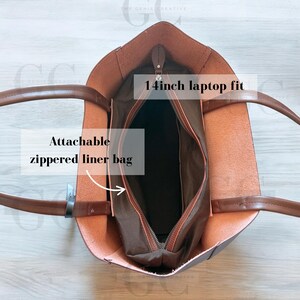 May include: Brown leather tote bag with a zippered liner bag. The bag is open to show the interior, which is lined with a dark brown fabric. The bag has a 14 inch laptop fit.