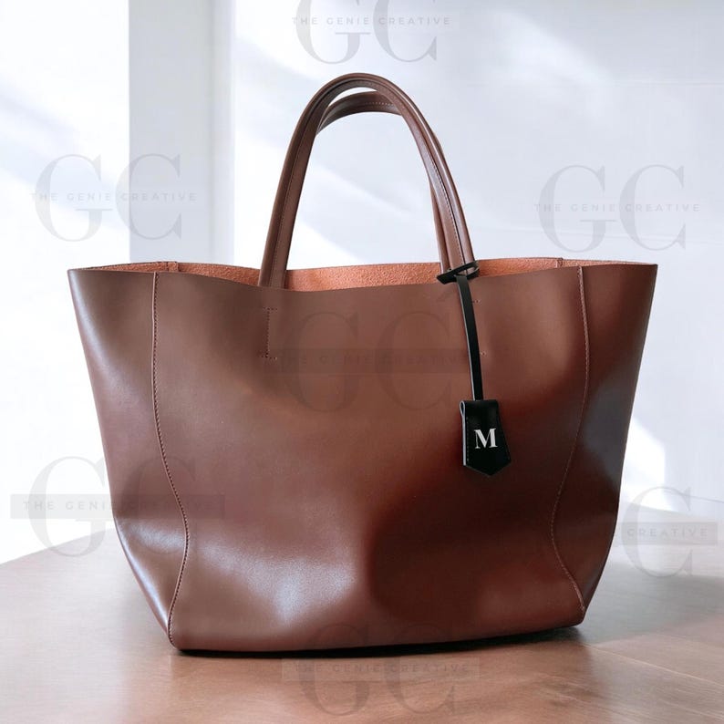 May include: A brown leather tote bag with a black leather tag that says "M" on it.