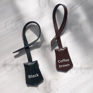 May include: Two leather keychains with a pointed tag. The keychain on the left is black with the word "Black" printed on the tag. The keychain on the right is brown with the words "Coffee brown" printed on the tag.