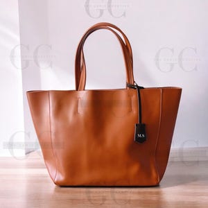 May include: A brown leather tote bag with a black leather strap and a black leather tag that says "M.S."